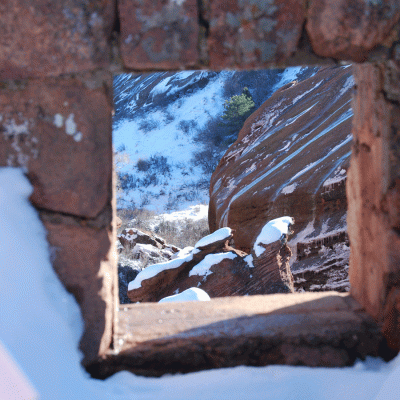 Window square made by red rocks in Colorado, surrounded by snow and in the background more rocks and base of a mountain
