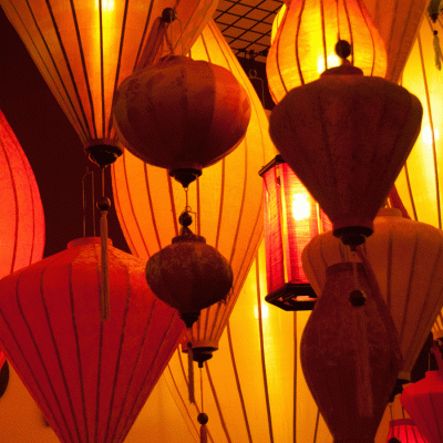 I large group of lighted lanterns are spreading a yellow and orange shine with dramatic shadows. The image is inviting and warm in its tones.