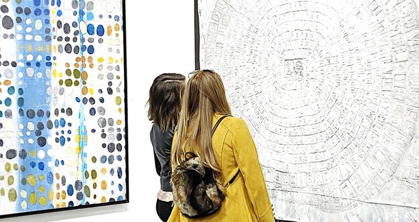 Two women at an art fair look at a large artwork from Gebhardt Gallery