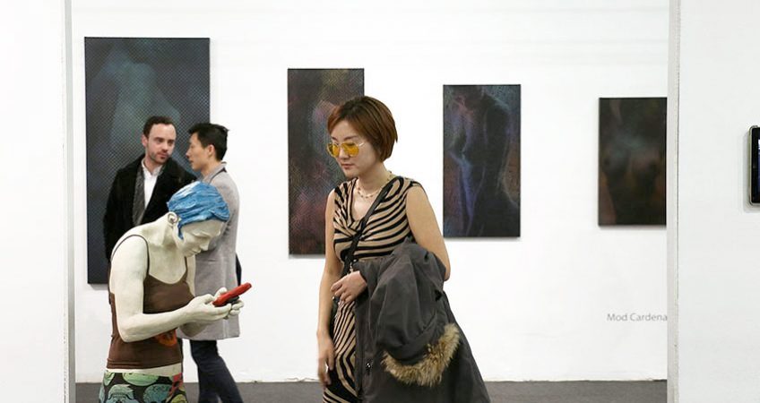 An art collector at an art fair is looking at an original life-size sculpture of a woman on their smartphone